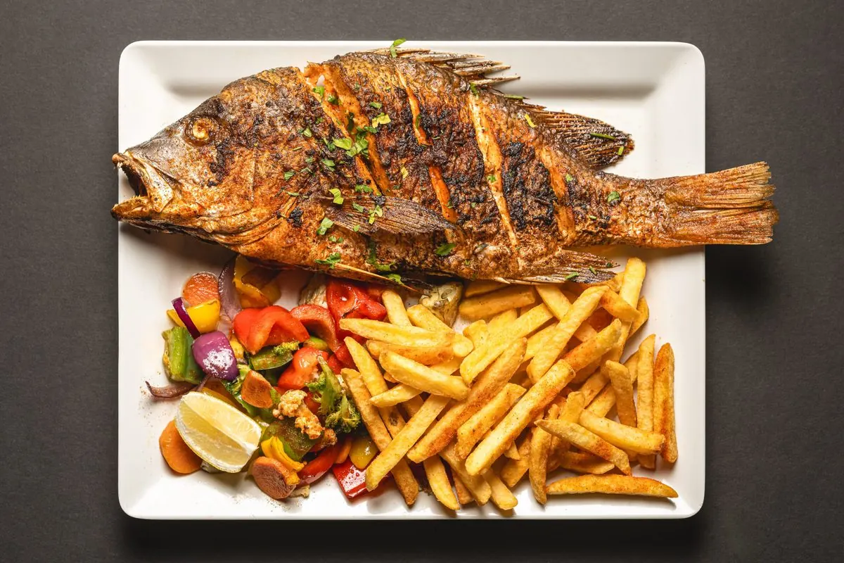 A whole grilled fish with chips, lemon and roasted vegetables